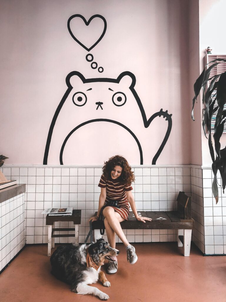 Smiling woman with her dog inside a stylish cafe with artistic wall decor.